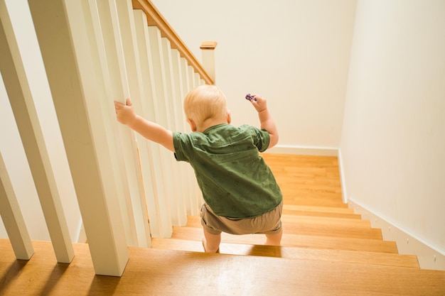 Ragazzo bambino con vista posteriore che scende le scale di legno Ragazzino che usa le scale da solo per la prima volta Crescendo ragazzo coraggioso e sicuro di sé