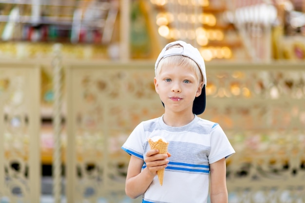 Ragazzo bambino felice che cammina in un parco di divertimenti e mangia il gelato