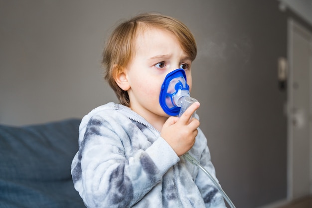 Ragazzo bambino malato che fa l'inalazione a casa, facendo l'aerosol di terapia utilizzando un nebulizzatore