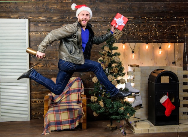 Ragazzo barbuto in movimento salto Consegna regalo di Natale Ancora tempo Servizio di consegna Consegna regali Uomo cappello da babbo natale fretta di consegnare il regalo in tempo Natale sta arrivando Diffondere felicità e gioia