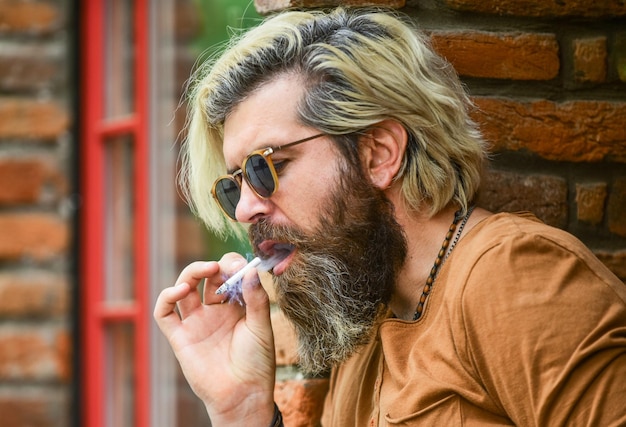 Ragazzo barbuto stile casual cattiva abitudine concetto dannoso per la tua salute fumo dipendente dalla nicotina è un forte fumatore uomo barbuto con gli occhiali rilassarsi con la sigaretta brutale hipster maturo che fuma sigaretta