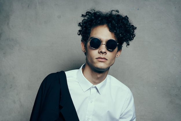 Ragazzo bello con i capelli ricci con una camicia bianca e una giacca su uno sfondo grigio ritratto di studio fotografico foto di alta qualità