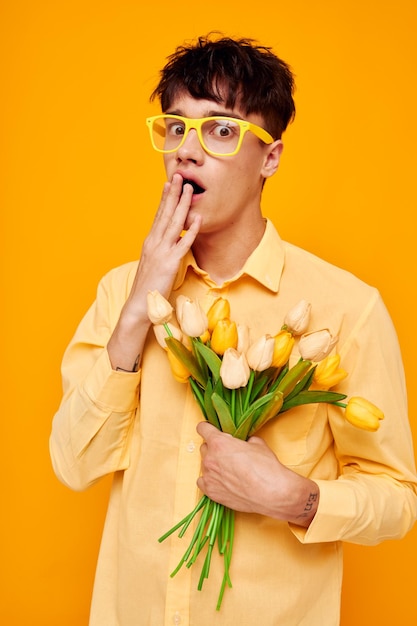 Ragazzo bello dare fiori indossare occhiali camicia gialla sfondo isolato inalterato