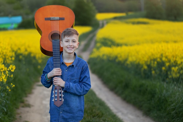 Ragazzo bello del ritratto con la chitarra che cammina sulla strada dell'estate. Giovane musicista sulla strada del successo.