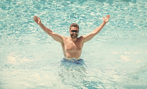 Ragazzo bello felice in occhiali da sole che nuota in piscina durante la festa in piscina estiva