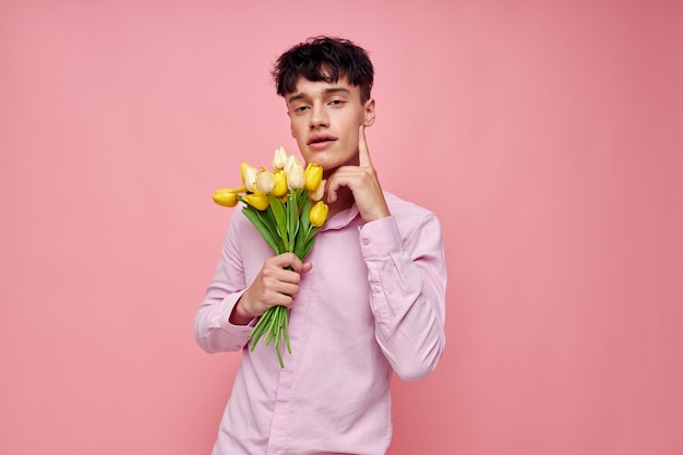 Ragazzo bello in una camicia rosa con un mazzo di fiori che gesturing con le sue mani ha isolato lo sfondo inalterato