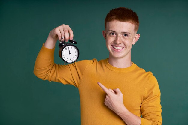 Ragazzo bianco con la testa rossa che tiene in mano la sveglia e la indica