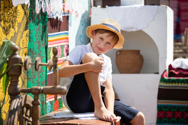 Ragazzo bielorusso o ucraino con un cappello di paglia sullo sfondo della stufa. Bambino di campagna.