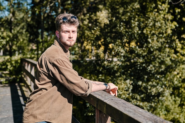 Ragazzo biondo appoggiato alla ringhiera di un ponte in una foresta che guarda dritto