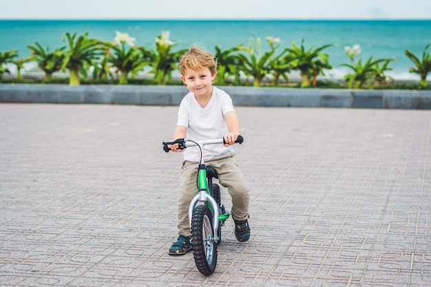 Ragazzo biondo attivo del bambino che guida la bicicletta nel parco vicino al mare