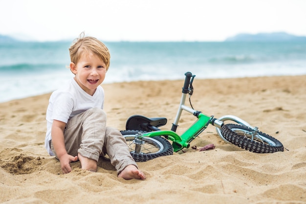 Ragazzo biondo attivo del bambino che guida la bicicletta nel parco vicino al mare