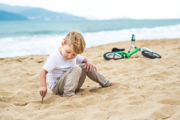 Ragazzo biondo attivo del bambino che guida la bicicletta nel parco vicino al mare