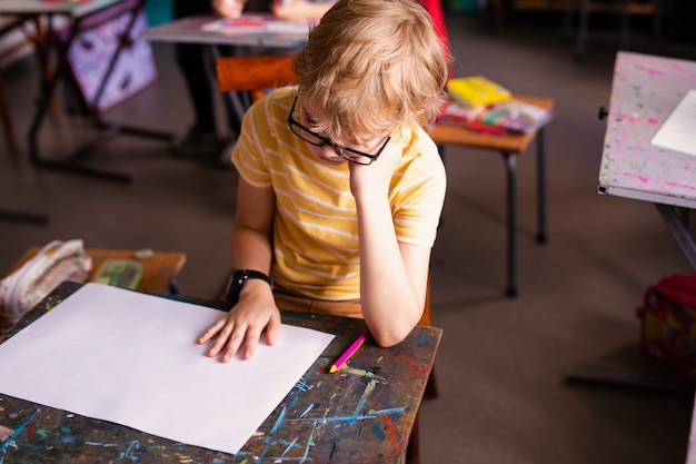 Ragazzo biondo con gli occhiali di disegno. Gruppo di alunni delle scuole elementari in aula sulla classe di arte