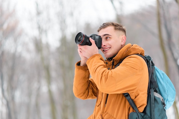 Ragazzo biondo della fotografia che spara agli alberi d'inverno con la neve mentre cammina nella foresta