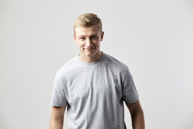 ragazzo biondo sorridente vestito con una t-shirt bianca in posa sullo sfondo bianco in studio