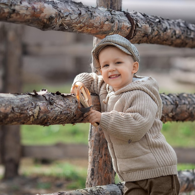 Ragazzo bullo ragazzo con una fionda mira a qualcuno vicino a una recinzione nel villaggio all'aperto Rustico bambino a piedi nudi ragazzo con un cappello spara una fionda