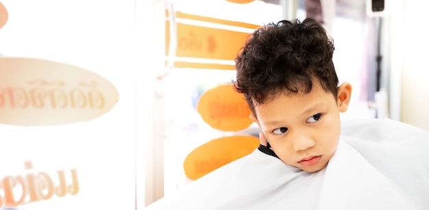 Ragazzo carino bambino asiatico che ottiene capelli tagliati dal parrucchiere al parrucchiere. Cura dei capelli e concetto di stile di vita dell'infanzia.