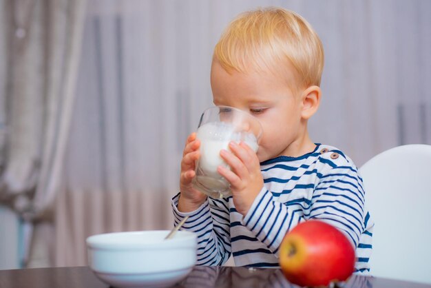 Ragazzo carino bambino che fa colazione Alimentazione del bambino Mangiare sano Bambino che fa uno spuntino Alimentazione sana Bere latte Bambino tenere un bicchiere di latte Bambino carino ragazzo sedersi a tavola con piatto e cibo Cibo sano