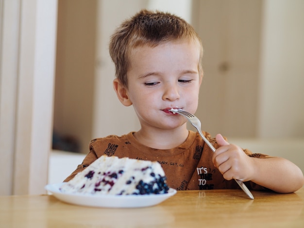 Ragazzo carino bambino che mangia una torta a casa