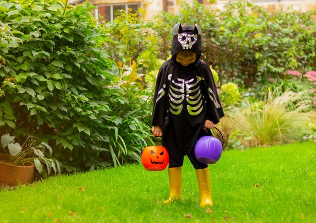 Ragazzo carino bambino in un costume da pipistrello per Halloween sul prato con secchi di zucca per dolci