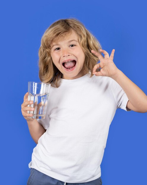 Ragazzo carino che beve acqua fresca isolata sullo sfondo dello studio il ragazzino tiene un bicchiere d'acqua in miniera