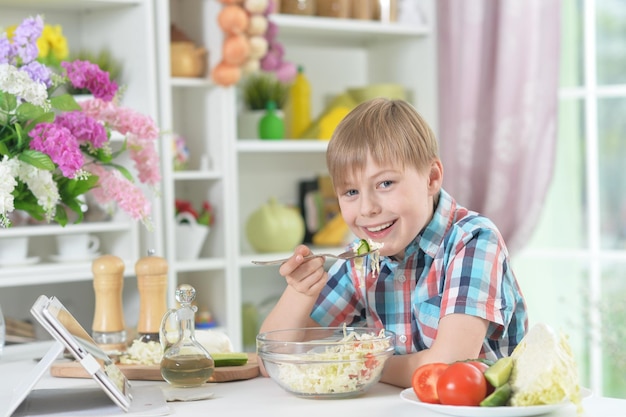 Ragazzo carino che mangia insalata sana in cucina