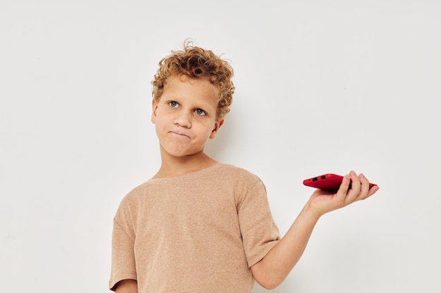 Ragazzo carino con capelli ricci in possesso di uno sfondo chiaro telefono rosso