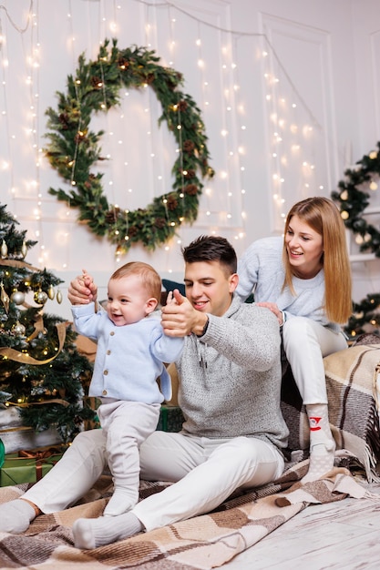 Ragazzo carino con genitori felici vicino all'albero di Natale Una famiglia con un bambino piccolo in una camera da letto vicino a un albero di Natale decorato Atmosfera festiva di Capodanno Celebrazione in famiglia