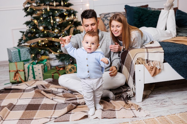 Ragazzo carino con genitori felici vicino all'albero di Natale Una famiglia con un bambino piccolo in una camera da letto vicino a un albero di Natale decorato Atmosfera festiva di Capodanno Celebrazione in famiglia