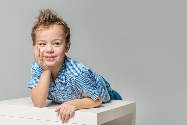 Ragazzo carino con una camicia blu al tavolo su uno sfondo grigio isolato