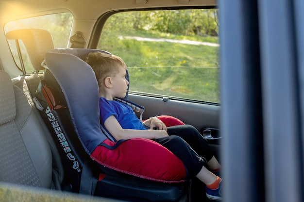 Ragazzo carino di 3-4 anni in età prescolare seduto nel seggiolino per auto e piangere durante il viaggio con la famiglia in auto