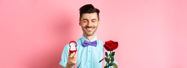 Ragazzo carino di San Valentino che fa proposta di matrimonio mostrando anello di fidanzamento in piccola scatola e r rossa