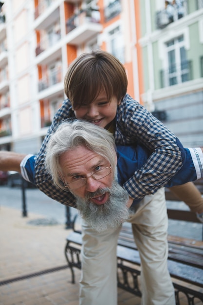 Ragazzo carino divertirsi con il nonno sulle spalle cavalcando per le strade della città