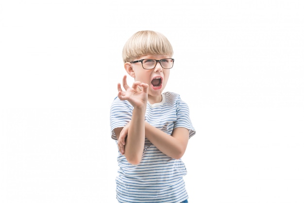 Ragazzo carino emotivo mostrando ok o pollice in su. Adorabile bambino su sfondo isolato. Lo studio ha sparato di scolaro.