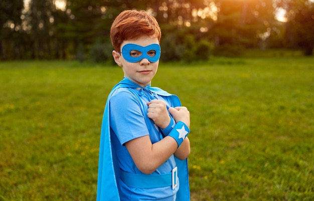 Ragazzo carino in abito da supereroe che guarda l'obbiettivo nel parco verde