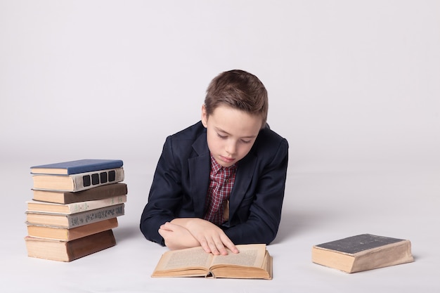 Ragazzo carino in un vestito si trova e legge un libro su uno sfondo bianco.