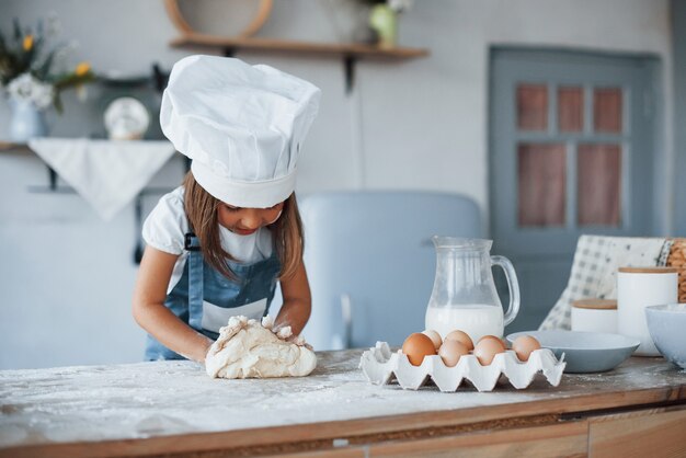 Ragazzo carino in uniforme bianca da chef che prepara il cibo in cucina.