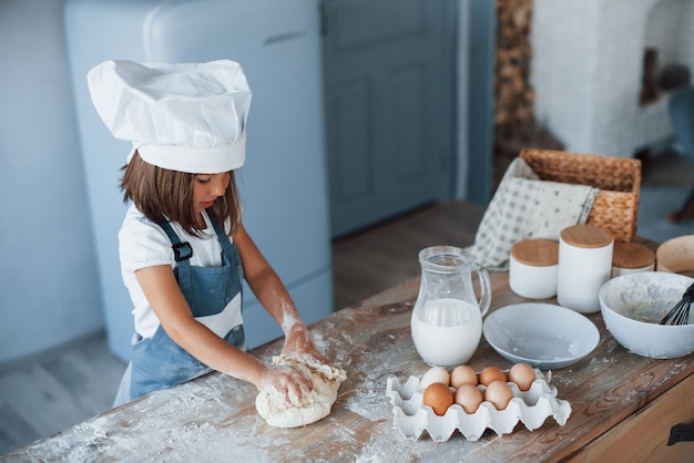 Ragazzo carino in uniforme bianca da chef che prepara il cibo in cucina.