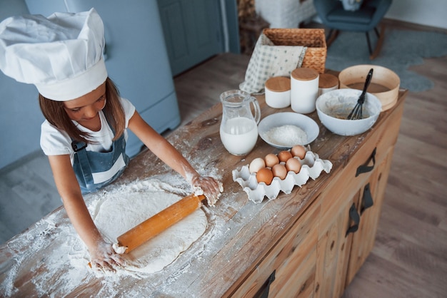 Ragazzo carino in uniforme bianca da chef che prepara il cibo in cucina.