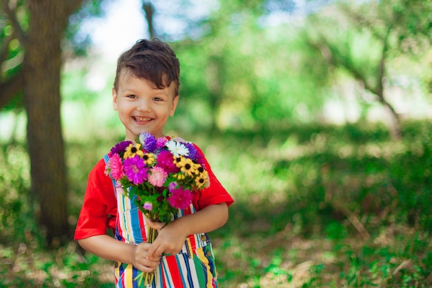 Ragazzo carino riccio con un mazzo di fiori un bambino in una maglietta rossa con fiori di campo luminosi