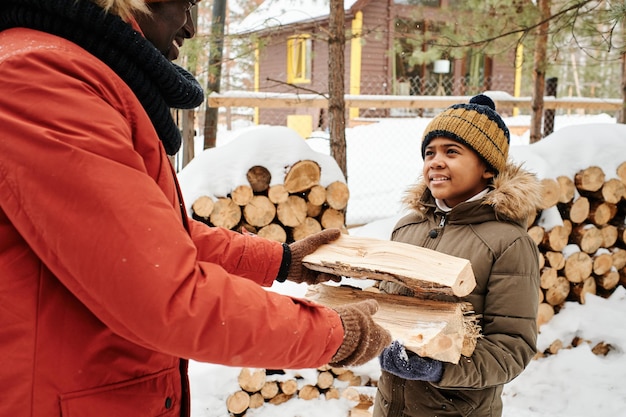 Ragazzo carino sorridente con piccoli tronchi di legno che guarda suo padre mentre lo aiuta