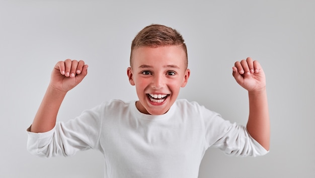 Ragazzo carino su uno sfondo grigio alzò le mani dicendo sì, vincitore, buona fortuna.