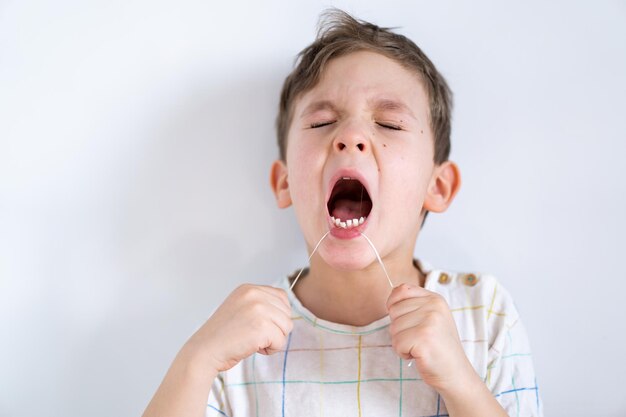 Ragazzo carino tirando dente sciolto utilizzando un processo di filo interdentale per rimuovere un dente da latte