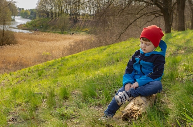 Ragazzo carino un ragazzo di quattro anni si siede su una collina su un tronco e guarda il lago. Turismo familiare verde, passeggiate con i bambini all'aperto