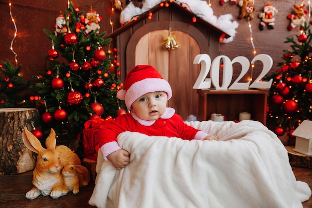 Ragazzo carino vestito da Babbo Natale si siede vicino all'albero di Natale. merci per bambini e vacanze. Concetto di Capodanno invernale. natale 2022