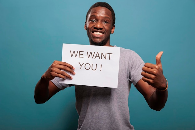 Ragazzo casual che usa un messaggio su carta per pubblicizzare un'offerta di lavoro davanti alla telecamera, dando opportunità di carriera al candidato di reclutamento in studio. Dipendenti delle risorse umane che reclutano persone per il colloquio.