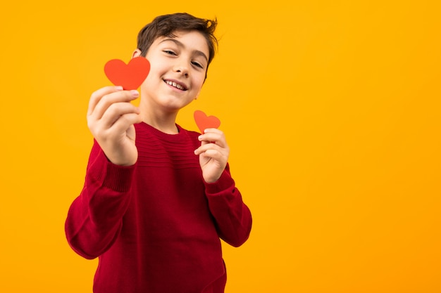 Ragazzo caucasico bello allegro divertente con le carte di carta sotto forma di cuori per l'arancia del onn di San Valentino