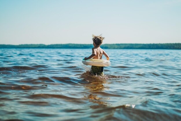 Ragazzo caucasico carino che corre nell'acqua con schizzi e risate Vacanze sul lato del mare Immagine dell'infanzia felice con il fuoco selettivo