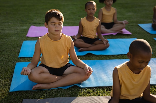 Ragazzo caucasico che pratica yoga e medita seduto sulla stuoia di yoga in giardino a scuola