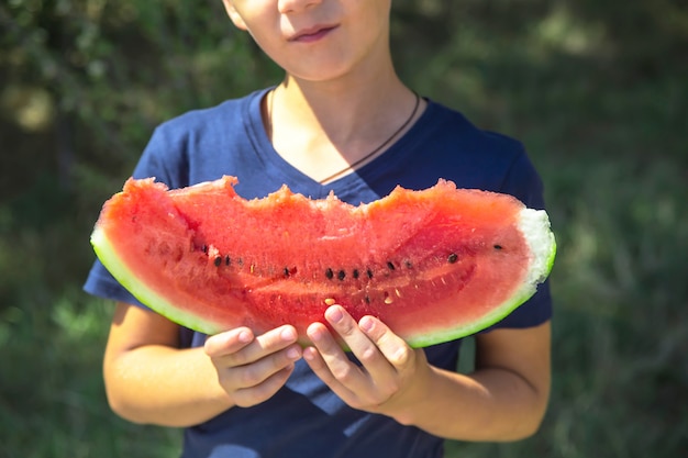 Ragazzo caucasico che tiene e che mangia una grande fetta pungente di anguria matura rossa